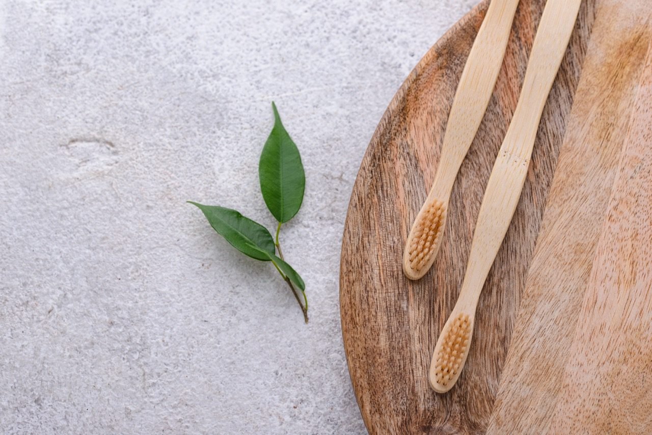 Two bamboo toothbrushes and fresh green leaves on a wooden board