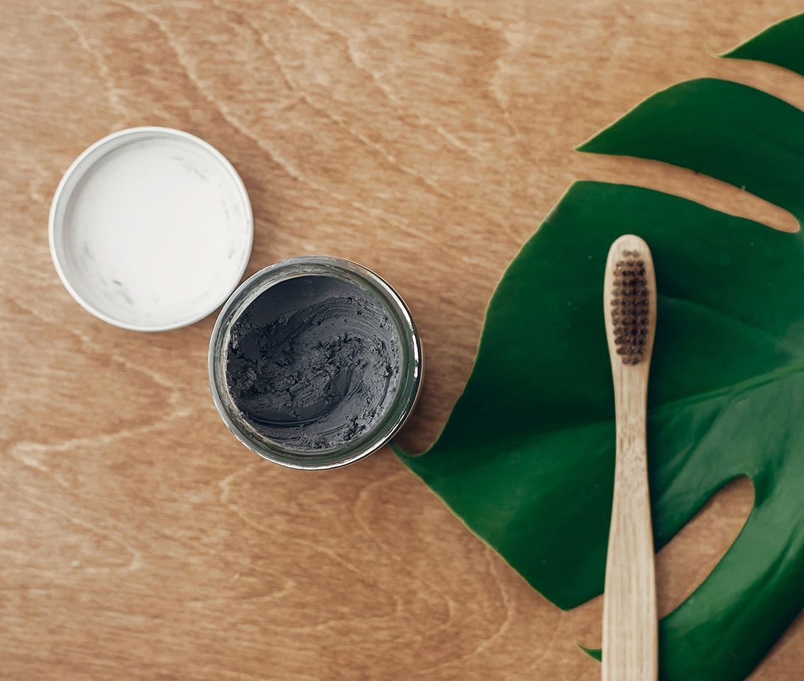 Bamboo toothbrush beside jars of natural tooth powder on a wooden surface